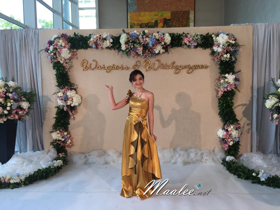 พร้อมเช่า ชุดราตรียาว ไหล่เฉียง สีทอง ปักเลื่อมไล่สี จับจีบแต่งโบว์ช่วงเอว ประดับดอกไม้สวยหวานบนไหล่