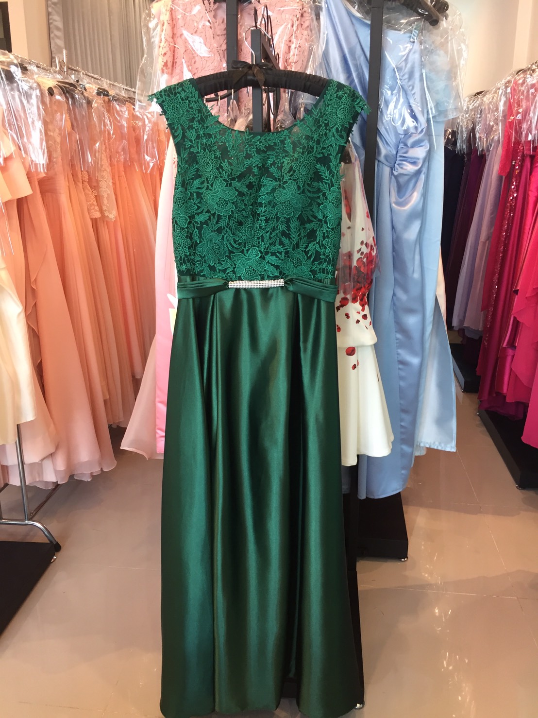 พร้อมเช่า ชุดราตรียาว แขนกุด สีเขียว อกแต่งลูกไม้ กรโปรงเนื้อผ้ามัน คาดเอวคริสตัล เซ็กซี่ผ้าหลัง เพิ่มเข็มกลัดโบว์ช่วงหลัง