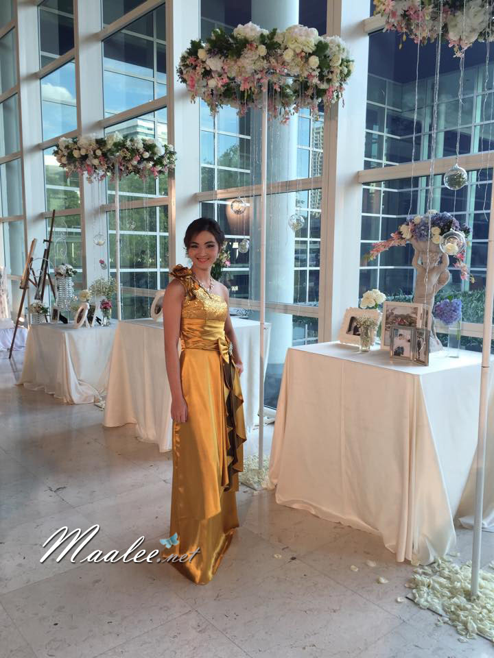 พร้อมเช่า ชุดราตรียาว ไหล่เฉียง สีทอง ปักเลื่อมไล่สี จับจีบแต่งโบว์ช่วงเอว ประดับดอกไม้สวยหวานบนไหล่