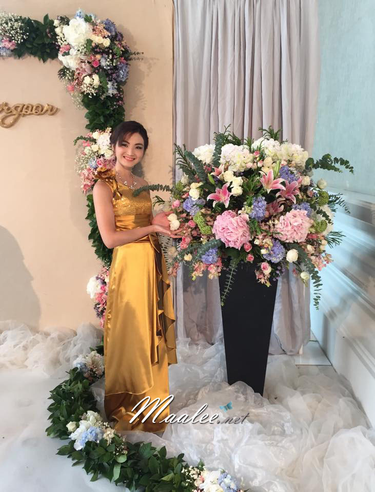 พร้อมเช่า ชุดราตรียาว ไหล่เฉียง สีทอง ปักเลื่อมไล่สี จับจีบแต่งโบว์ช่วงเอว ประดับดอกไม้สวยหวานบนไหล่